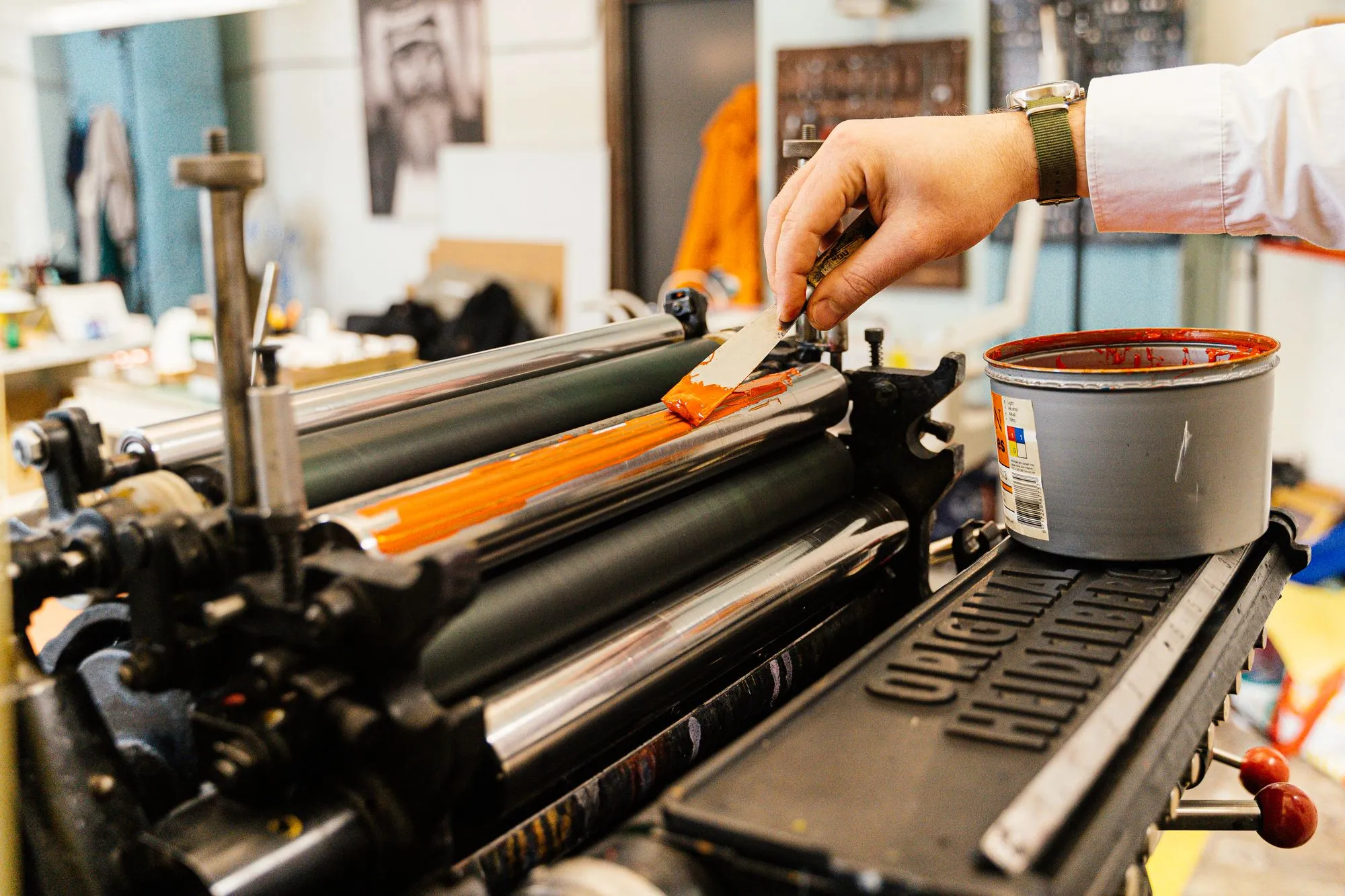 A hand rolling orange ink across the rollers of a letterpress