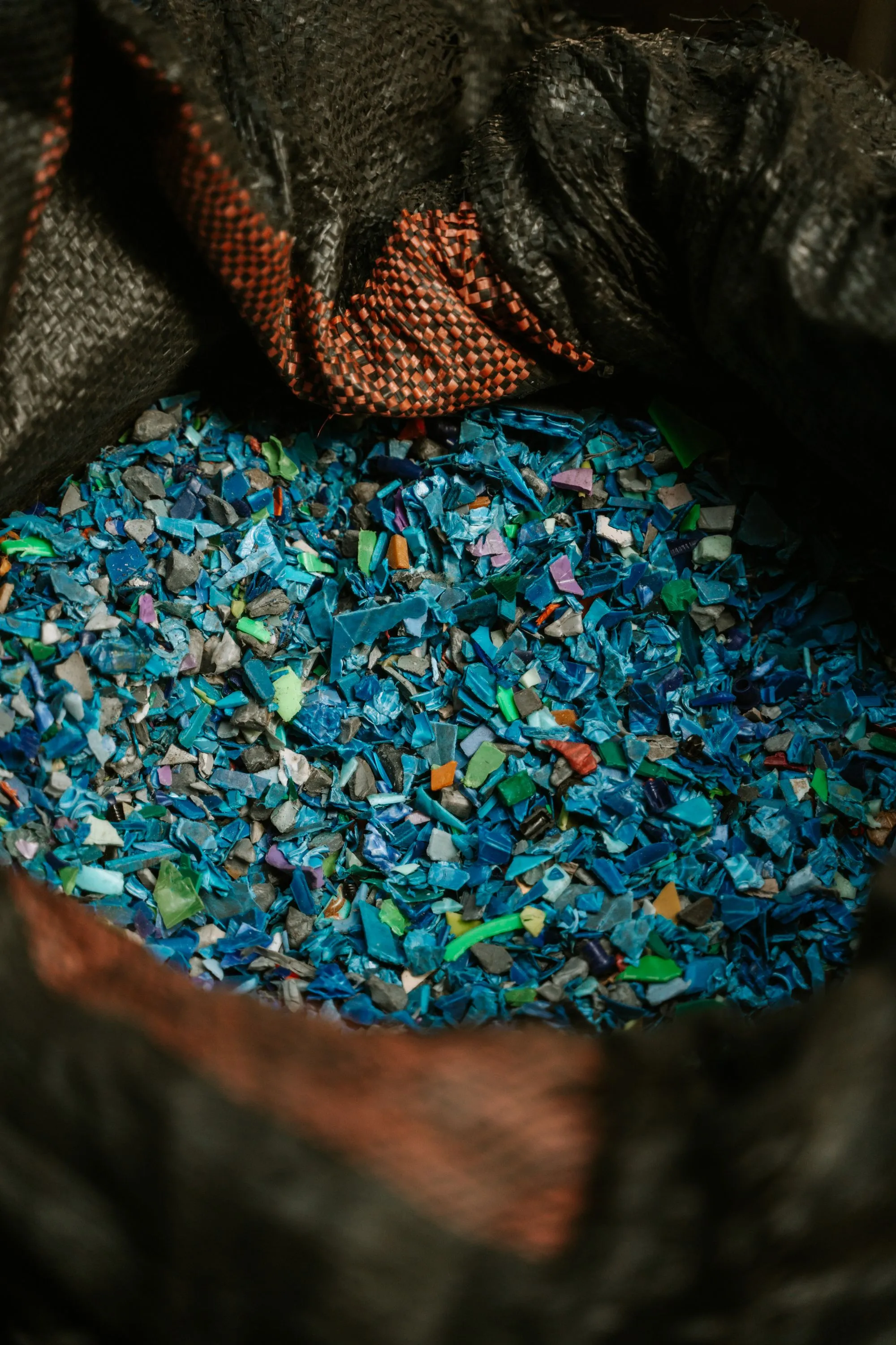 Coloured plastic granulate filling a woven sack, mostly blues and greys