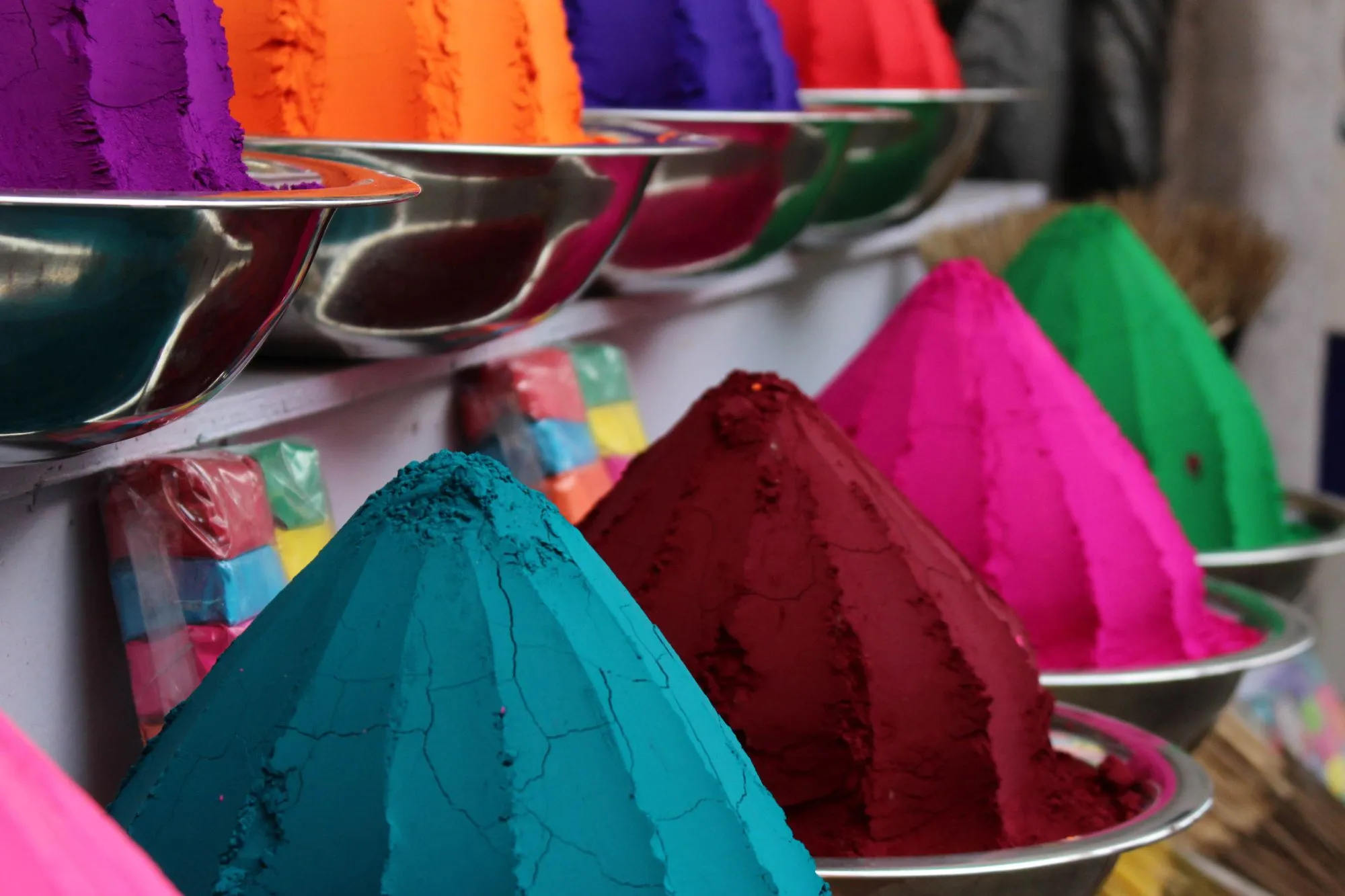 Cones of pigment powder in teal, crimson, magenta and green, each in a steel bowl